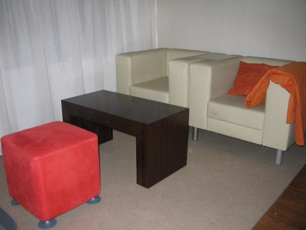 Dunkler Holztisch und zwei weiße Sessel und ein roter Hocker 